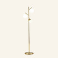 Slim brushed brass floor lamp with three opal white glass globes on angled branch arms, rising from a round metal base on cream backdrop.