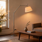 Swing arm floor lamp glowing warmly beside a walnut coffee table and linen sofa in a sunlit living room at golden hour.