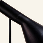Close-up of the matte black enamelled metal shade and pivot joint, showing fine grain texture and the slim cylindrical arm of the task lamp