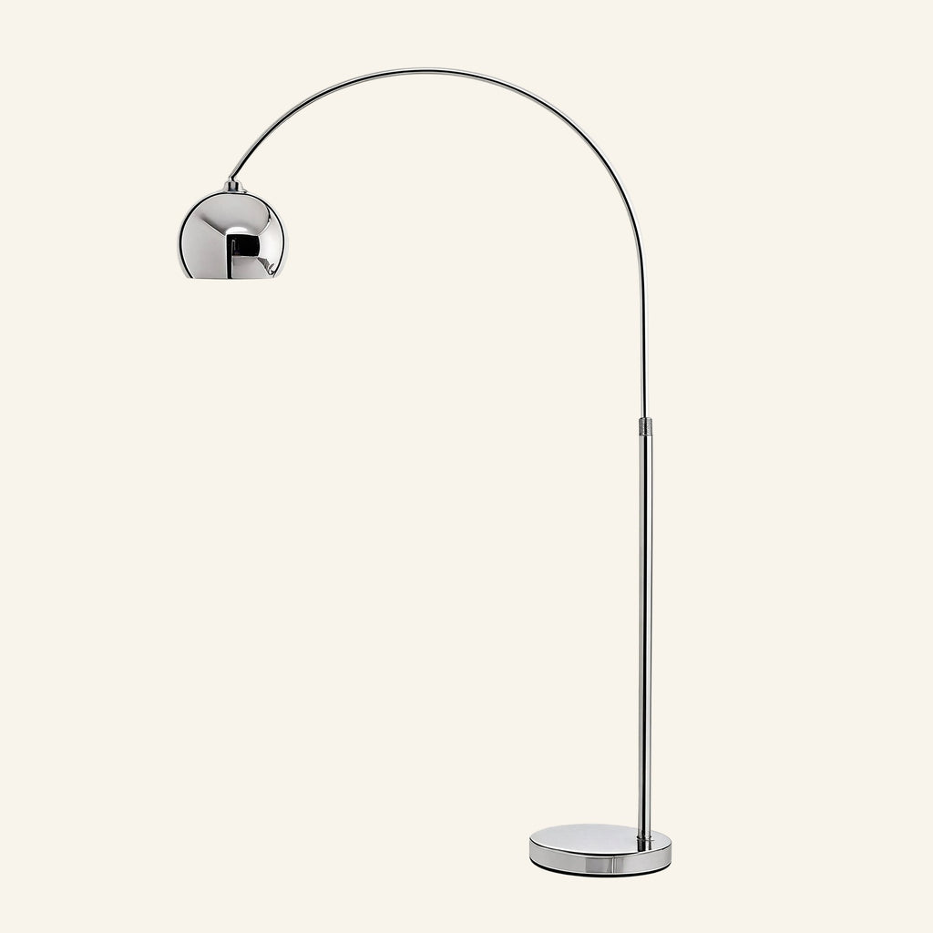 Polished chrome arc floor lamp with slender curving stem, hemispherical dome shade, and round mirrored base on cream studio backdrop