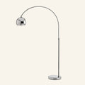 Polished chrome arc floor lamp with slender curving stem, hemispherical dome shade, and round mirrored base on cream studio backdrop