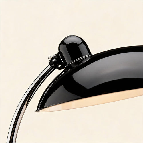 Close-up of the lacquered black dome shade and bulb housing meeting the polished chrome arm, showing reflective metal finish and pivot detail.
