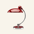 Oxblood-red lacquered dome shade and matching base accent paired with a polished chrome arm, Bauhaus desk lamp on neutral backdrop.