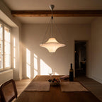 Saucer-shaped glass pendant glows above an oak dining table set with figs and wine, beneath exposed wooden ceiling beams at golden hour