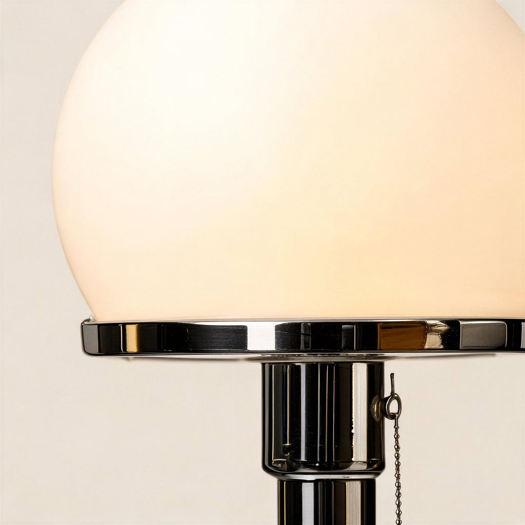 Close-up of the opal glass dome glowing warmly above a polished chrome collar and pull-chain socket on the lamp stem