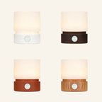 Four colour variants of the cordless mini table lamp arranged in a grid, frosted shades glowing warmly above white, black, terracotta and wood-grain bases