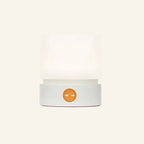 Front view of the cordless LED mini lamp in white, frosted shade lit warmly above a rounded base with glowing amber touch button