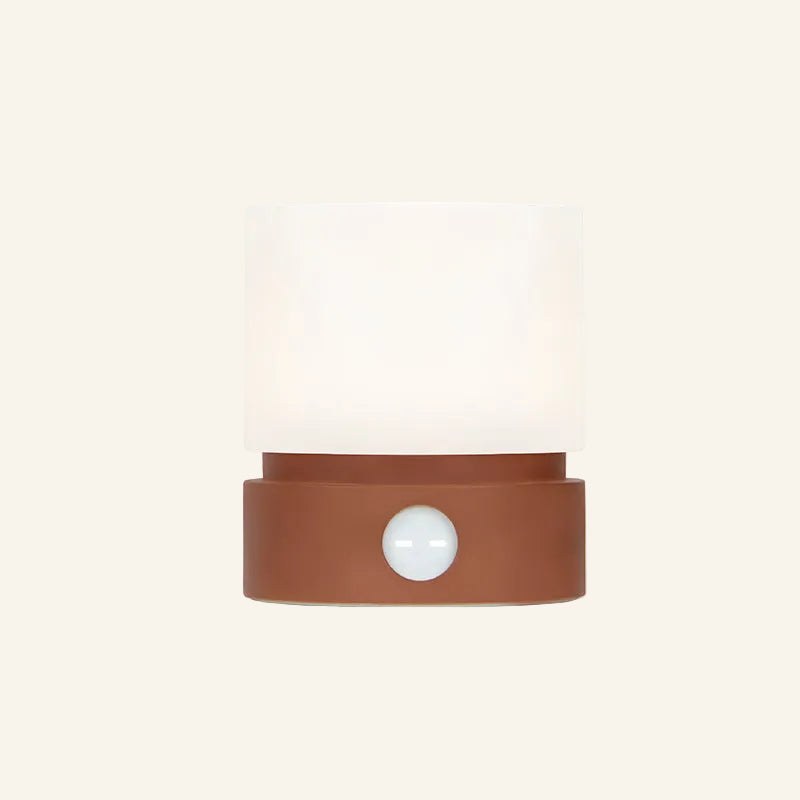 Front view of the cordless mood lamp in terracotta red, softly lit frosted shade above a rounded ceramic-look base with circular button