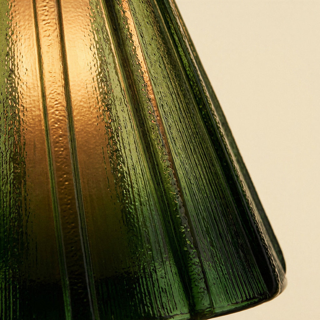 Close-up of the textured pleated glass shade showing deep green ribs fading to amber where warm light passes through.
