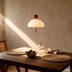 Lit pendant lamp hanging above a wooden dining table with woven placemats, fig bowl and wine glass in sunlit dining room