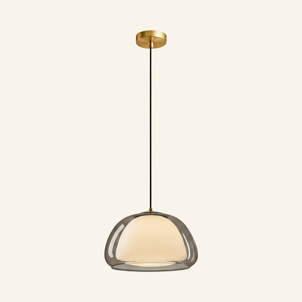 Side view of pendant lamp with smoke-tinted outer glass and warm opal core hanging from slim black cord and brass mount
