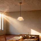 Pendant glowing above a wooden dining table with fig bowl and wine glass, rattan chair and plaster walls bathed in afternoon light