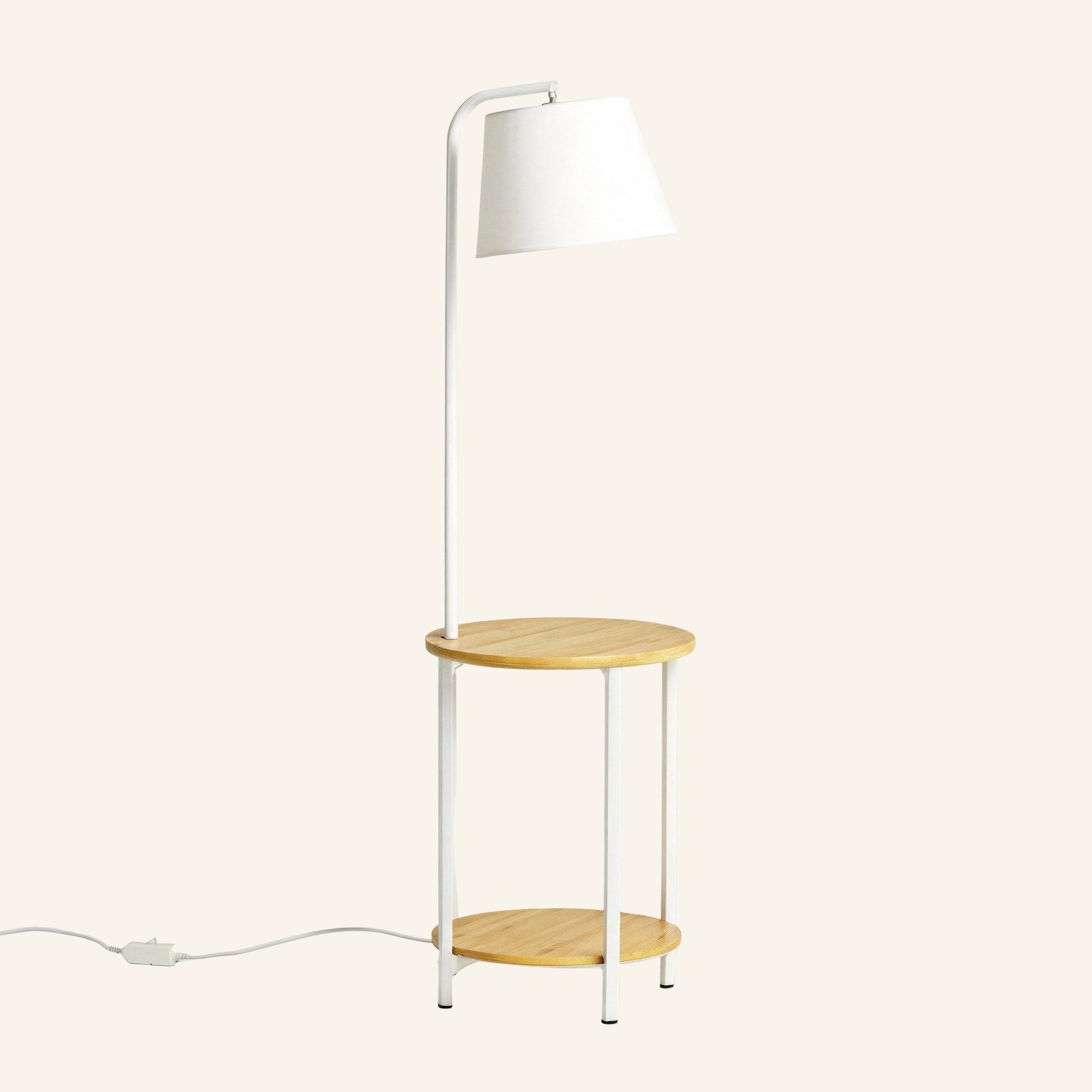 Slim white steel floor lamp with tapered fabric shade and two round bamboo shelves forming a built-in side table.