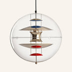 Clear glass globe pendant lamp on cream backdrop, polished metal hourglass diffuser stacked with blue and red reflector discs inside the sphere.