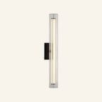 Slim vertical wall sconce with fluted clear glass column, matte black backplate, and brass center band housing a warm LED rod
