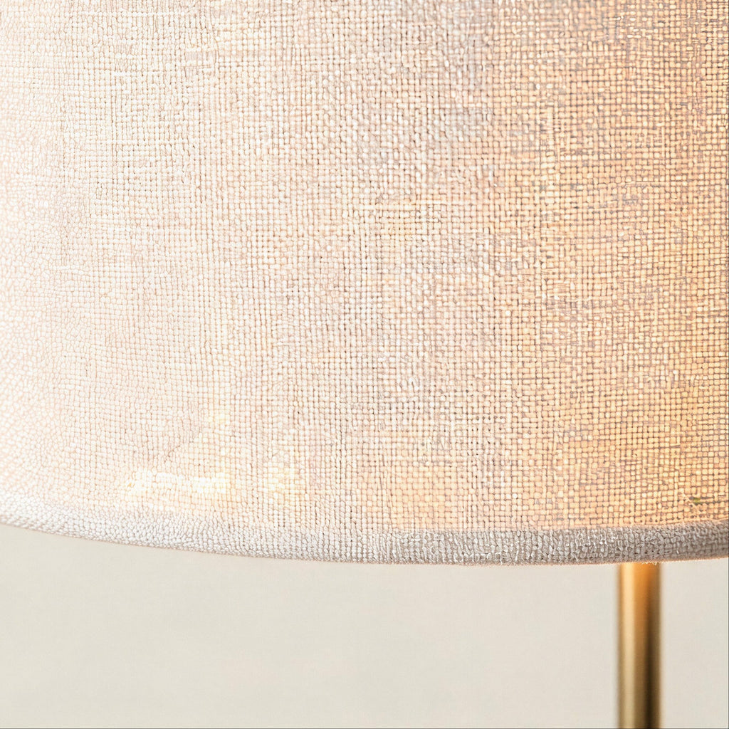 Close-up of the woven white linen drum shade showing textured weave and the gold metal stem rising from below.