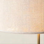Close-up of the woven white linen drum shade showing textured weave and the gold metal stem rising from below.