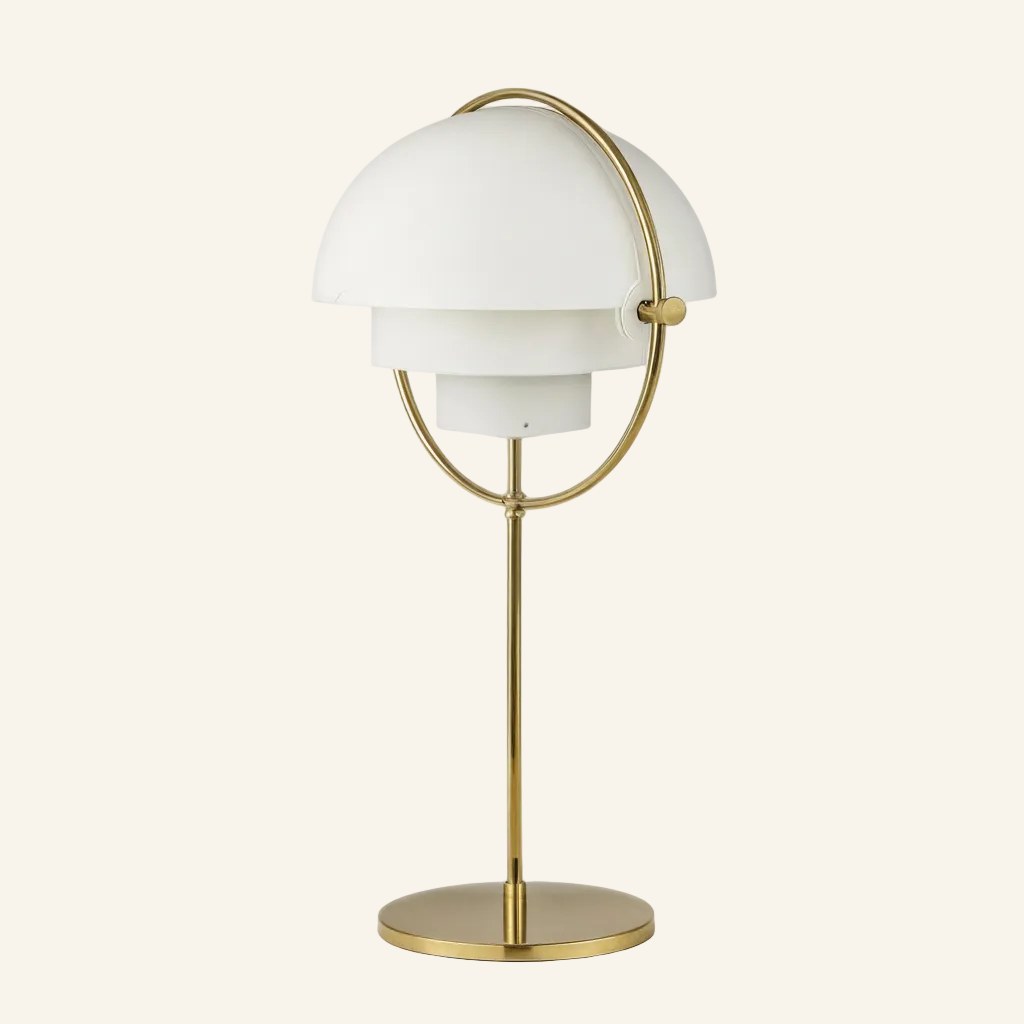 White twin hemispherical shades pivot inside a polished brass ring above a slim stem and disc base, mid-century table lamp on cream backdrop.