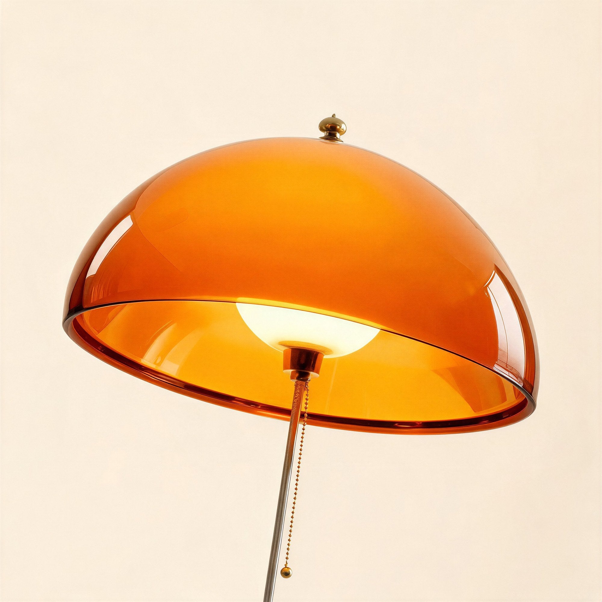 Close-up of the translucent amber acrylic dome shade, exposed bulb and brass beaded pull-chain against a soft cream backdrop
