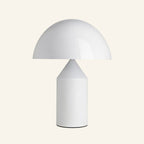 Glossy white mushroom dome table lamp with cylindrical metal base and inner cone reflector on cream studio backdrop