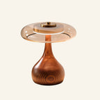 Teardrop wax-wood base supports an amber glass dome and brushed brass top-button cap on a cream studio backdrop, japandi table lamp