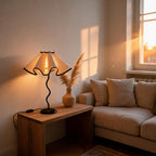 Lit lamp glows on a wooden side table beside a pampas-filled vase and beige sofa, warm sunset light pouring through the window.