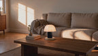 Cinematic video of a cordless mushroom table lamp glowing softly on a wooden coffee table beside books in a sunlit living room.