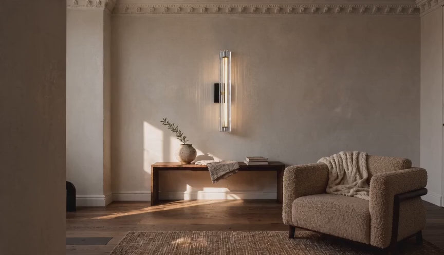 Cinematic video of a vertical fluted glass LED wall sconce glowing warmly above a wooden bench in a neutral living room.