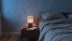 Cinematic video of a cordless linen shade table lamp glowing on a wooden nightstand beside a linen-dressed bed at dusk.