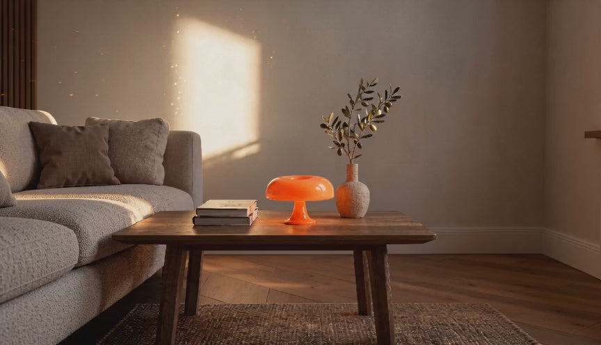 Cinematic video of an orange mushroom table lamp glowing on a wooden coffee table beside a sofa and olive sprig vase.