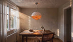 Cinematic video of a white glass dome pendant lamp with stacked orange acrylic rings glowing above a wooden dining table near a sunlit window.