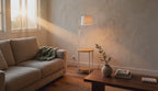 Cinematic video of a white-shade floor lamp with bamboo side-table shelves beside a sofa in a sunlit living room.