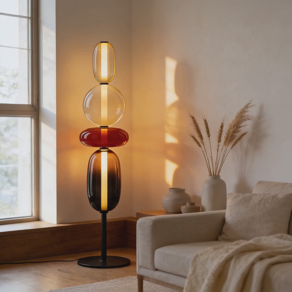 Cinematic video of a stacked glass pebble floor lamp glowing with amber, cherry and smoke tinted shades beside a sunlit window.
