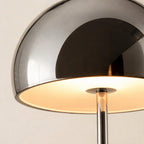 Close-up of the chrome dome shade reflecting soft light, warm bulb glow visible underneath above the slender mirrored stem
