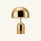 Brass-finish variant of the dome table lamp on cream background, golden polished shade above a tall cylindrical base with touch button
