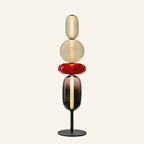 Stacked glass pebble floor lamp with amber, cherry red and smoke tinted shades on a black disc base, studio shot on cream background
