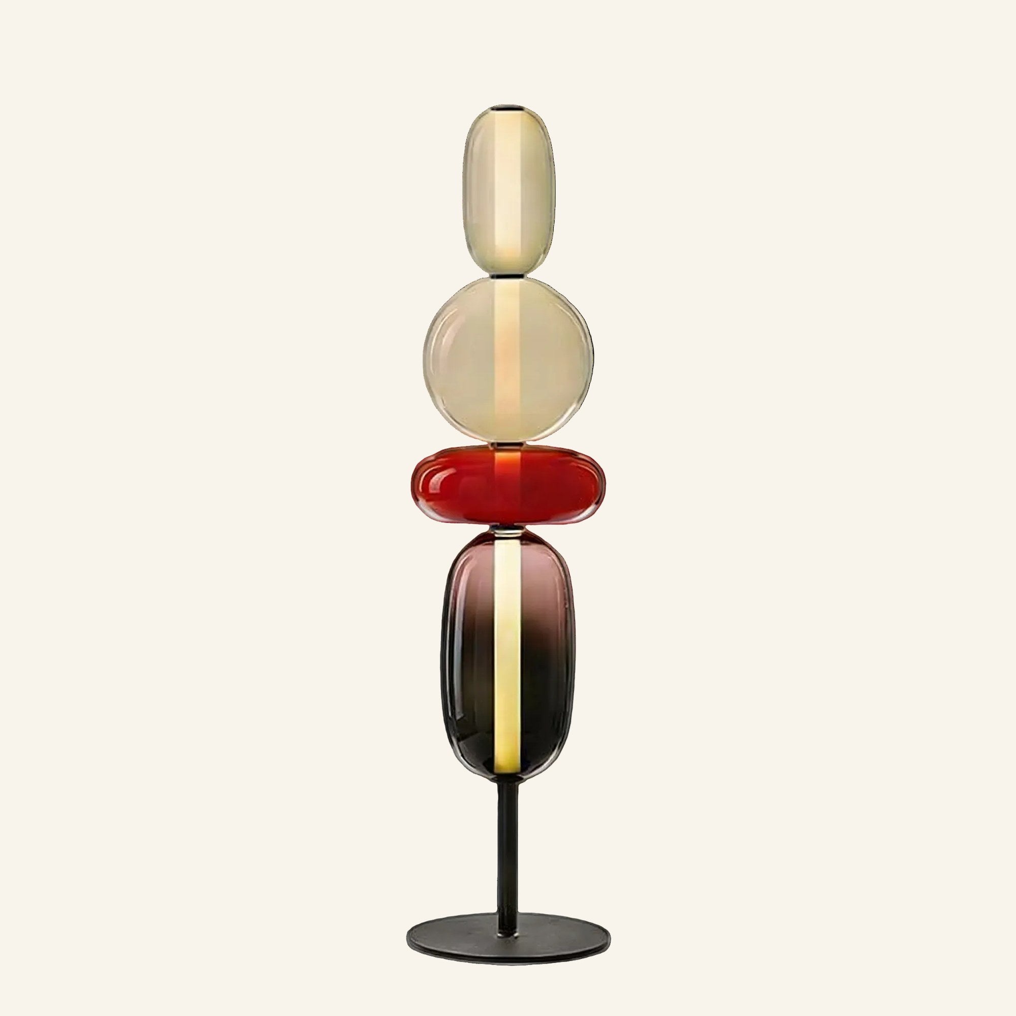 Stacked glass pebble floor lamp with amber, cherry red and smoke tinted shades on a black disc base, studio shot on cream background