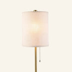 Close-up of the cylindrical linen drum shade glowing softly, revealing woven texture, brass cap, and beaded pull chain on the polished pole.