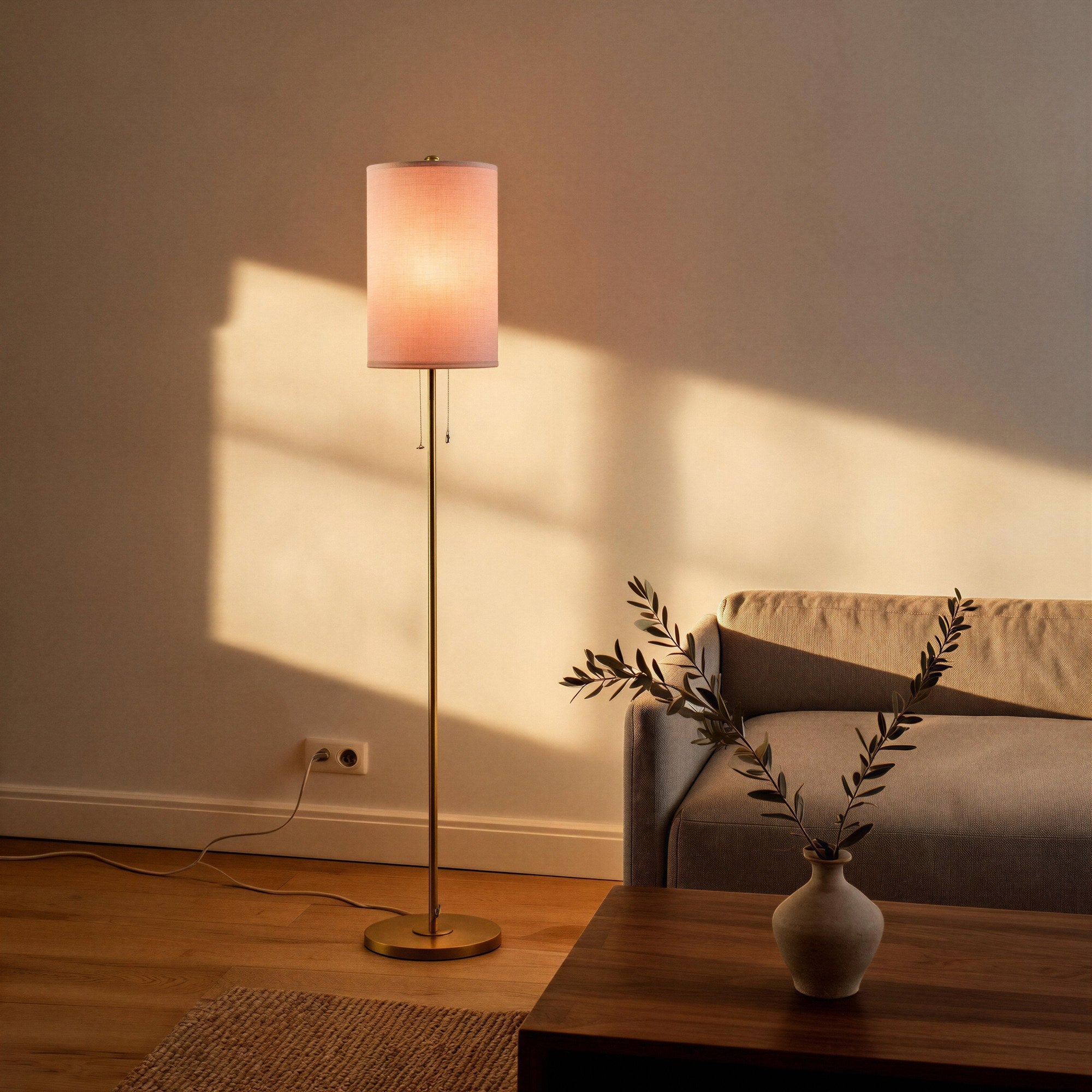 Lit floor lamp casting warm glow in a living room beside a linen sofa, walnut coffee table, ceramic vase with olive branch, and woven rug.