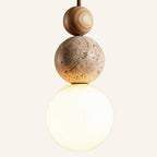 Side view of pendant light showing grained wood bead, beige travertine orb and softly lit opal glass globe stacked vertically.