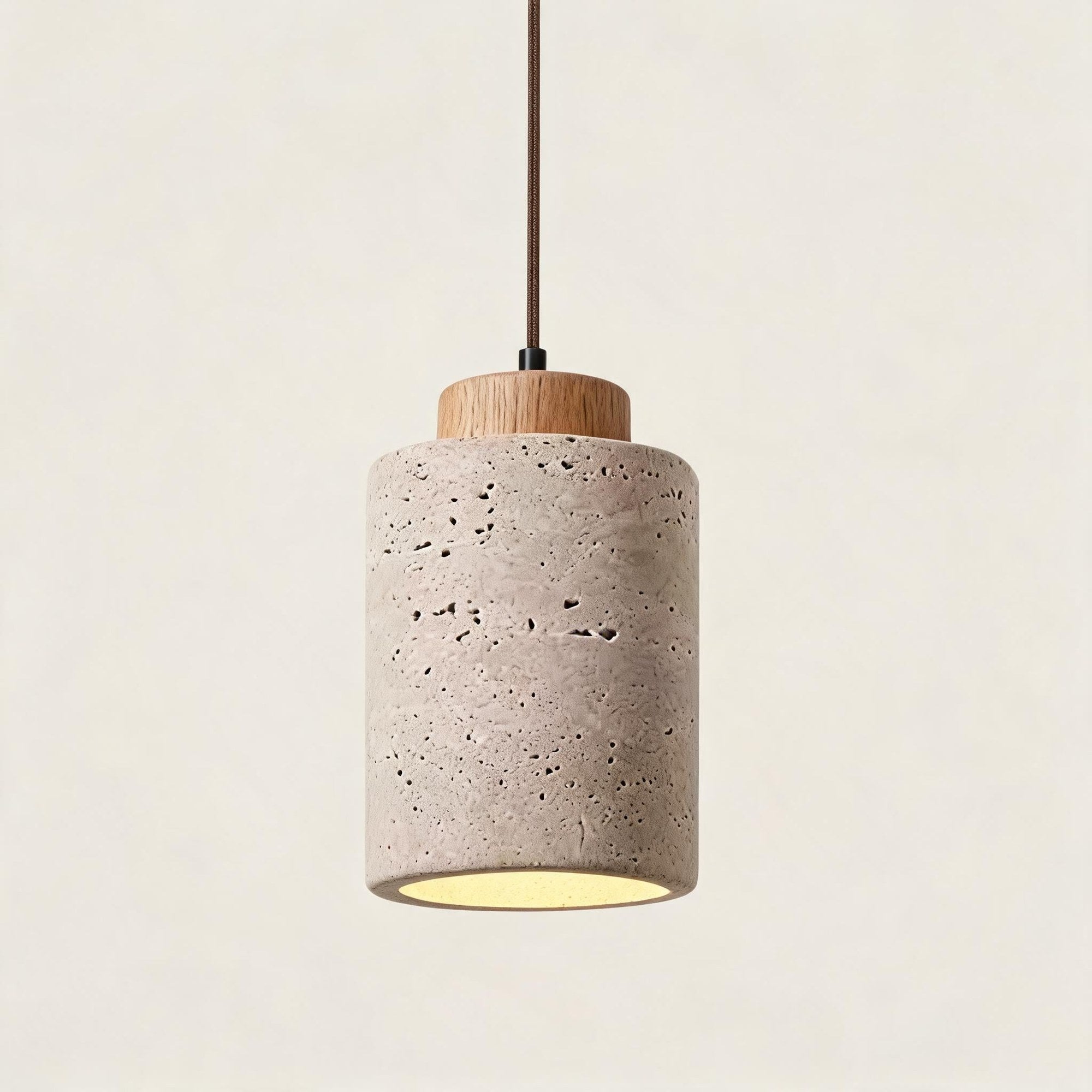 Studio shot of a mini cylinder pendant pairing pale travertine with a light oak collar, soft amber light spilling from the open base.