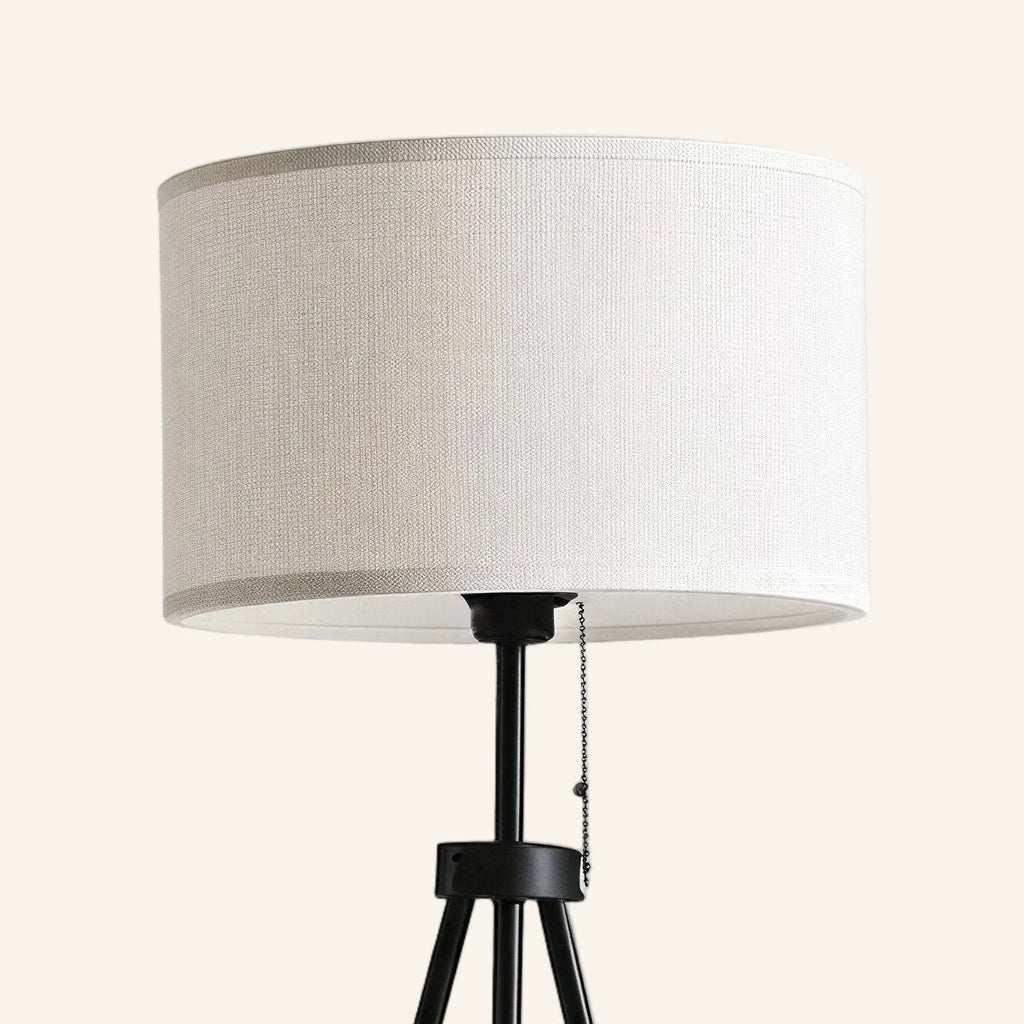 Close-up of the white linen drum shade meeting the black metal stem and pull-chain switch on a tripod floor lamp.
