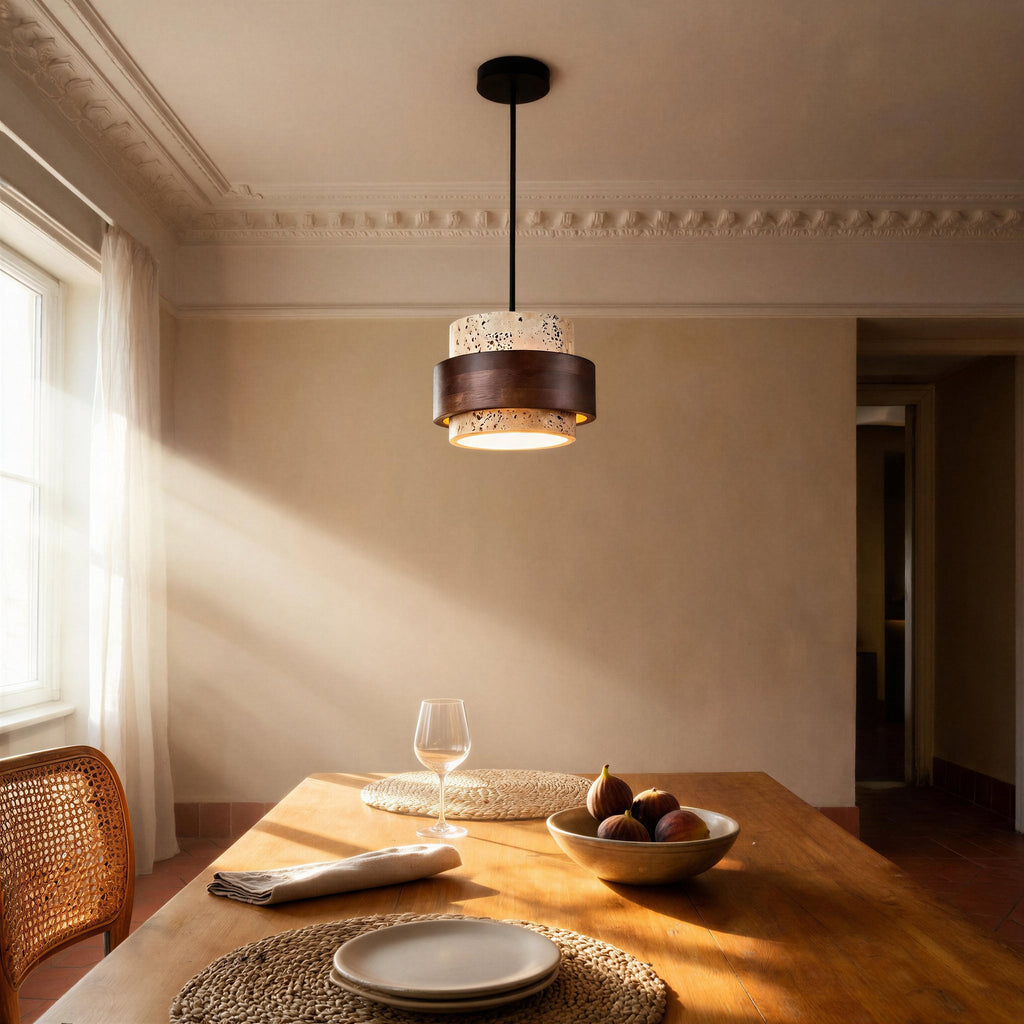Stone and walnut pendant glowing above a wooden dining table set with figs, plates and a rattan chair in a sunlit room.
